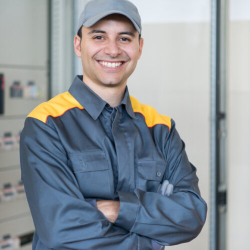 Portrait of a smiling electrician in front of an industrial electric panel in a factory Portrait of a smiling electrician in front of an industrial electric panel in a factory